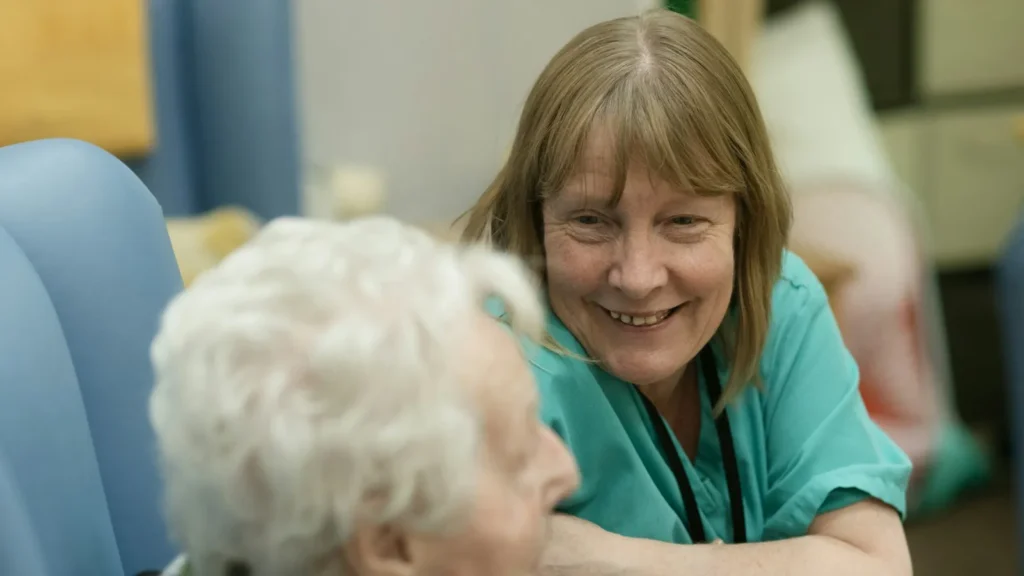 Smiling caregiver in scrubs talking with an older adult